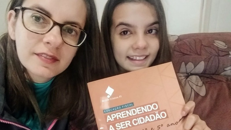 Foto de Gabriela com sua filha, mostrando o livro "Educação fiscal - Aprendendo a ser cidadão".