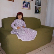Menina vestida de prenda, com vestido lilás, sentada no sofá