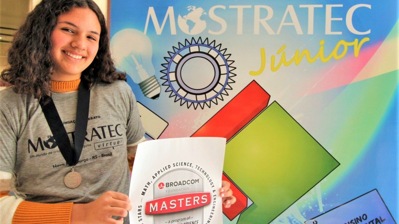 Monique apresentando a medalha e o cartaz que recebeu da Broadcom