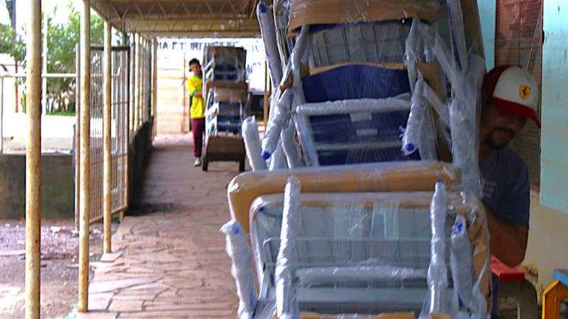 Foto que mostra dois entregadores, carregando uma pilha de cadeiras escolares que foram entregues na Escola Guarani, de Canoas.