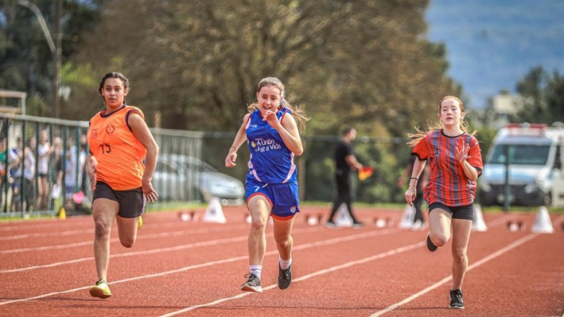 Três atletas jovens competindo em uma pista de atletismo.