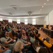 Auditório do Instituto de Educação, em Porto Alegre, com público atento a palestra da secretária da Educação, Raquel Teixeira, no palco, ao lado de bandeiras e um banner amarelo.