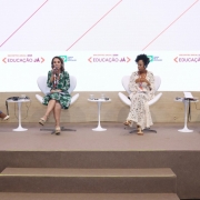 Raquel participando de um debate com mais três mulheres negras no Encontro Anual Educação Já 2025. Elas estão sentadas em cadeiras e um palco. Raquel fala ao microfone.