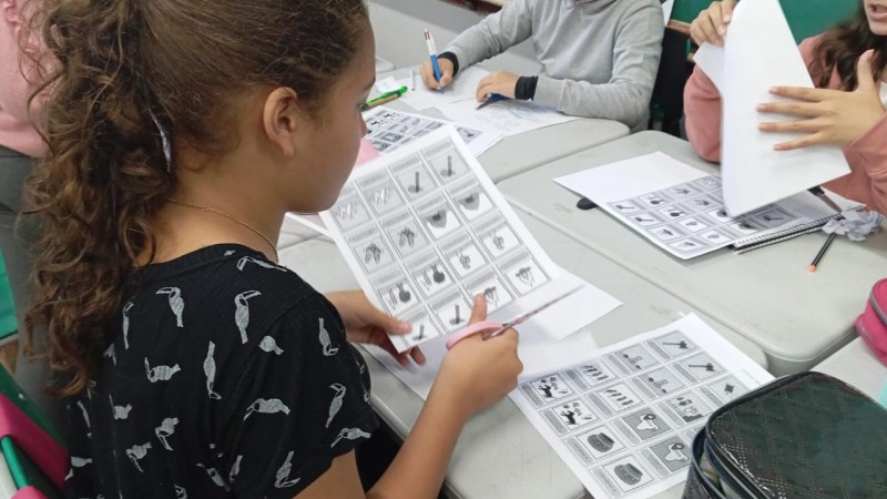Estudantes em sala de aula participam de atividade com recorte de figuras impressas em folhas