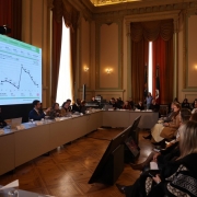 Foto do salão nobre do Palácio Piratini, em Porto Alegre, onde autoridades e convidados acompanham apresentação de dados projetados em telão. O encontro ocorre em ambiente formal, com decoração clássica e participação de representantes do governo e da sociedade.
