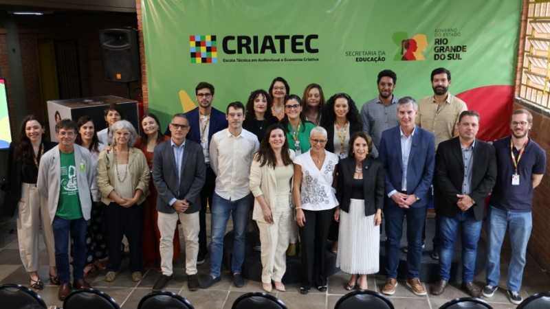 Foto de grupo registra o lan&ccedil;amento do plano de ocupa&ccedil;&atilde;o da Escola T&eacute;cnica CRIATEC, primeira voltada ao audiovisual e &agrave; economia criativa no Rio Grande do Sul. A imagem mostra autoridades, educadores e profissionais da cultura reunidos diante do painel institucional da CRIATEC, da Secretaria da Educa&ccedil;&atilde;o e do Governo do Estado do Rio Grande do Sul. Todos posam sorridentes em ambiente interno, com decora&ccedil;&atilde;o colorida e ilumina&ccedil;&atilde;o natural.