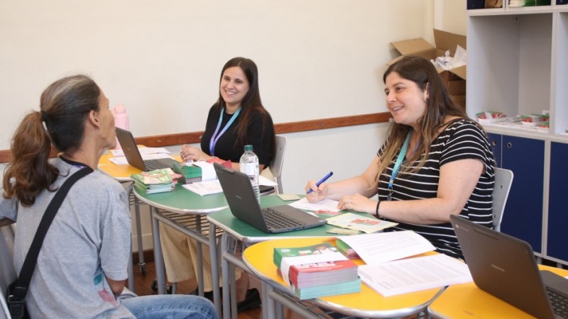 Foto mostra servidoras atendendo m&atilde;e de aluno.