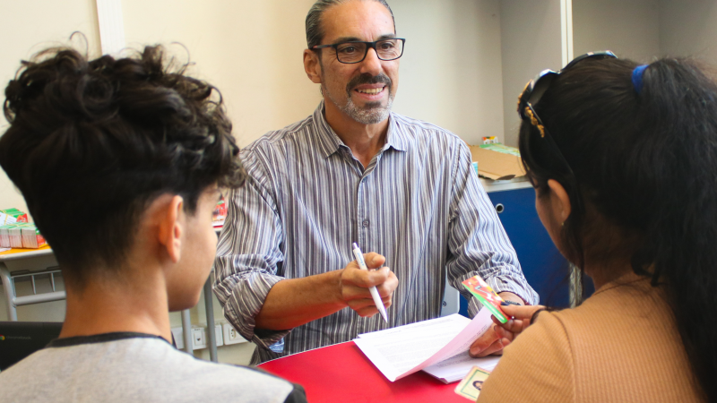 Foto mostra servidor entregando cart&atilde;o do Programa P&eacute; no Futuro &agrave; m&atilde;e e estudante.

