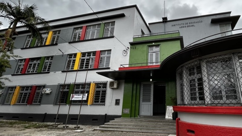Pr&eacute;dio de tr&ecirc;s andares com v&aacute;rias janelas e pintura nova, com uma grande porta branca na entrada. Acima, letreiro "Instituto de Educa&ccedil;&atilde;o Assis Brasil"


